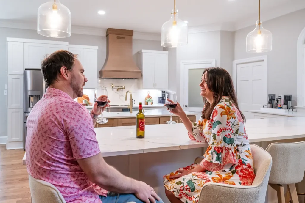 A man and woman enjoy red wine at a modern kitchen island remodeled by 7 Day Kitchens, with a wine bottle on the counter.