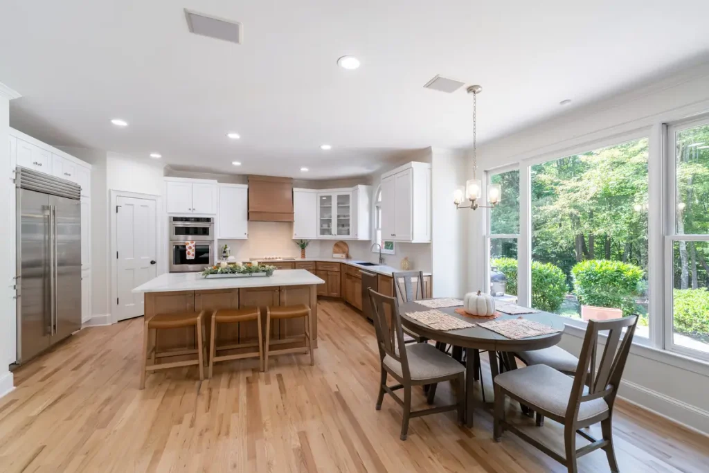 Recently remodeled by 7 Day Kitchens, this bright kitchen features white cabinets, a central island with wooden stools, and large windows.